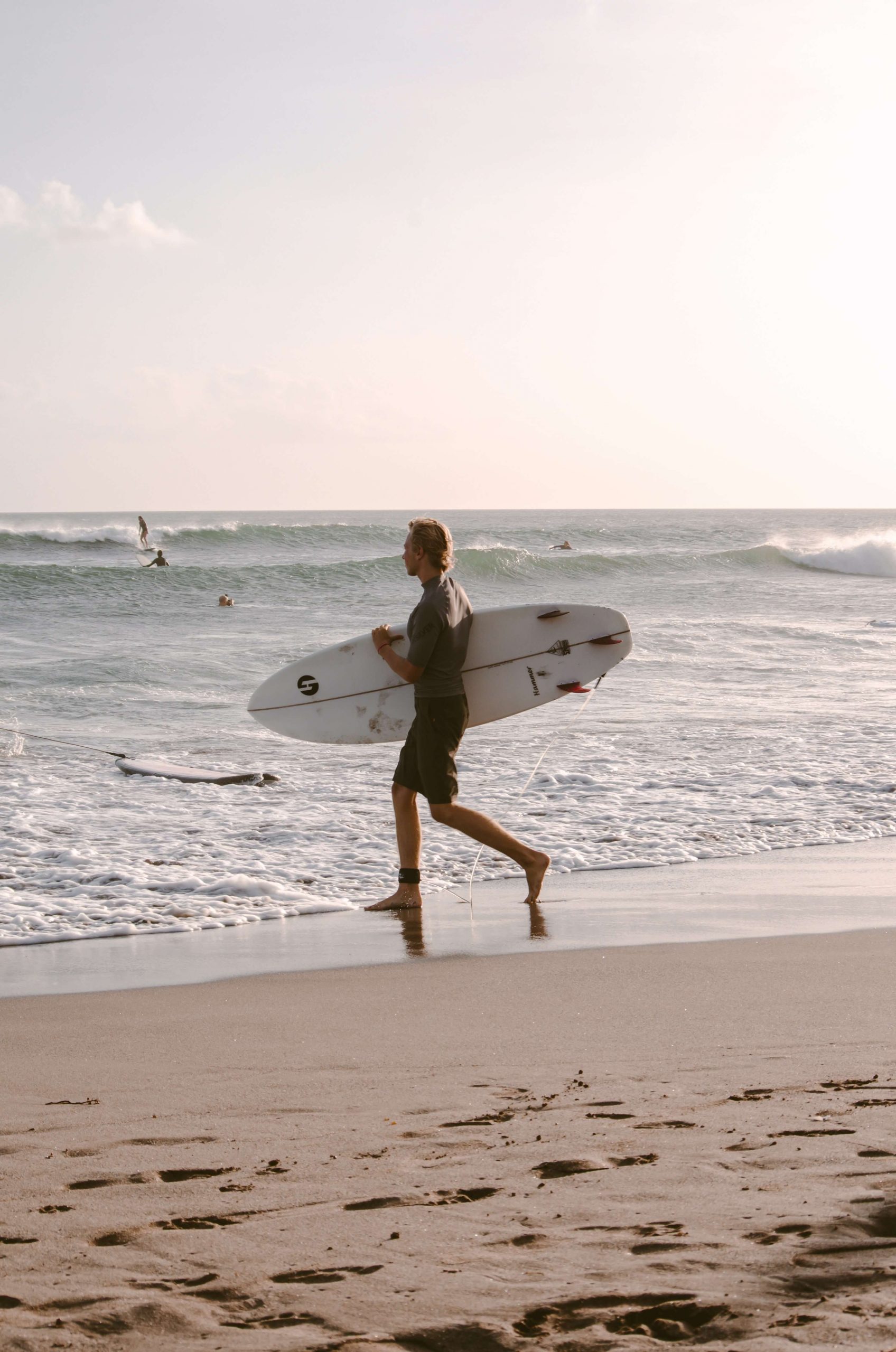 Male surfer holding short board walks towards the water.